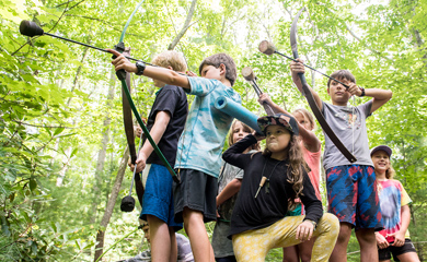 Summer campers playing archery games posing with bows on top of big boulder near Asheville