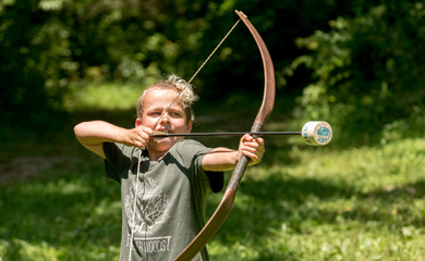 Boy with bow drawn with foam tipped arrow at summer day camp near Asheville