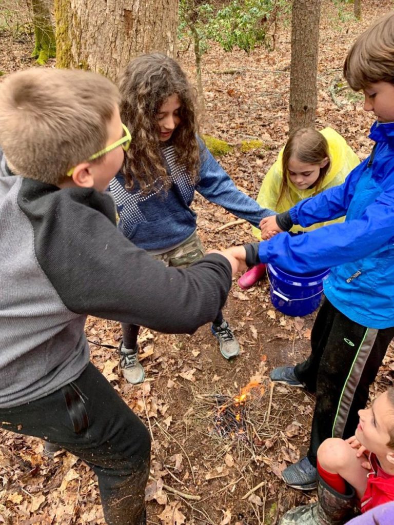 Children holding hands in a circle playing a game at nature camp