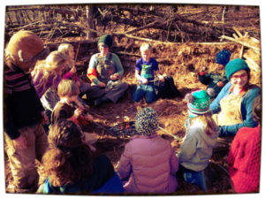 Children and counselors sitting in a circle in a primitive structure they made at nature camp