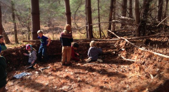 Children at afterschool nature program building the wall of a primitive structure in the forest