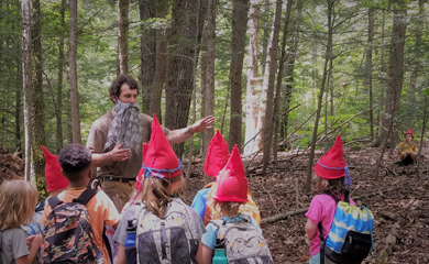 Group of children dressed as forest gnomes at day camp hearing story told by actor