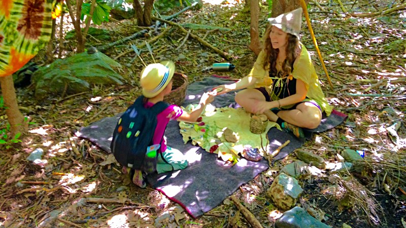 Nature school teacher and homeschool student sitting on blanket in woods doing some crafting