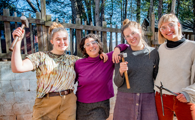 Four young women standing arm in arm with blacksmithing tools at blacksmithing day camp