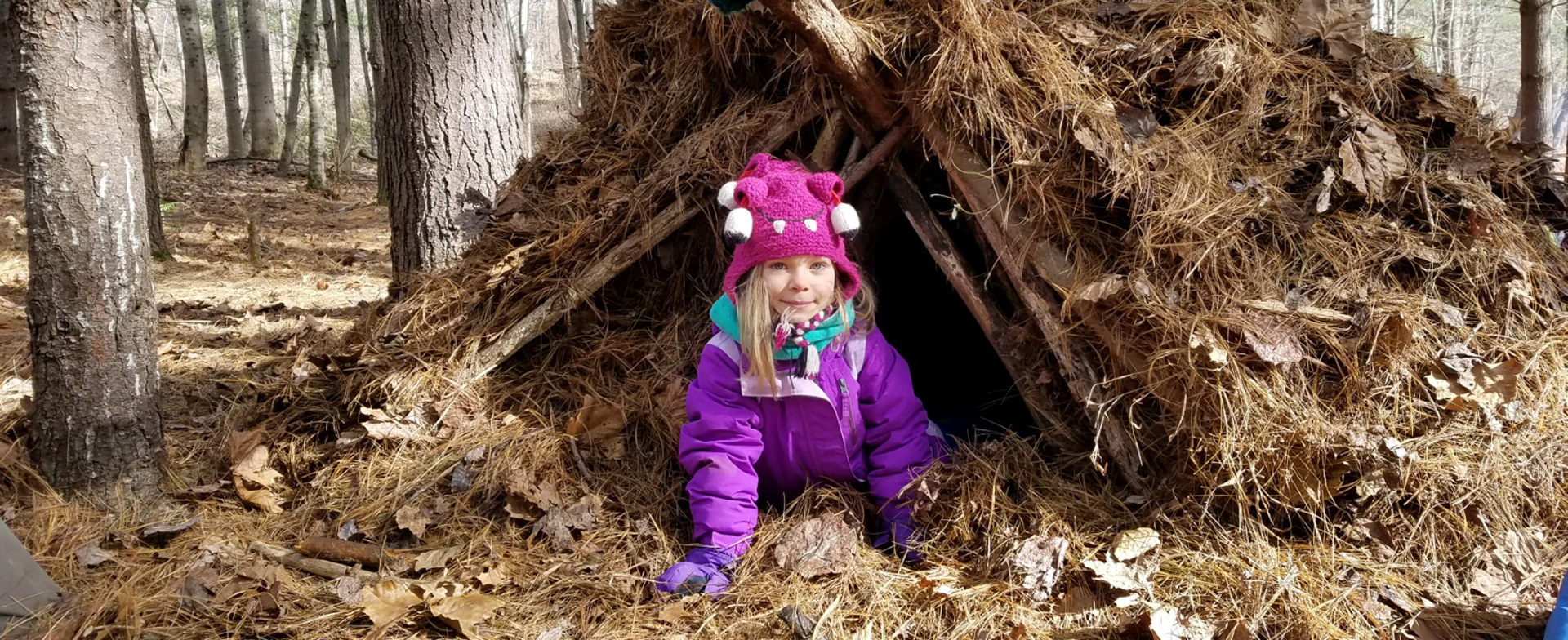 Girl crawling out of primitive structure in forest during winter homeschool nature class