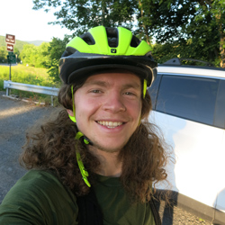 Griffin Harvey head shot wearing bright bicycling helmet with big smile and long curly hair