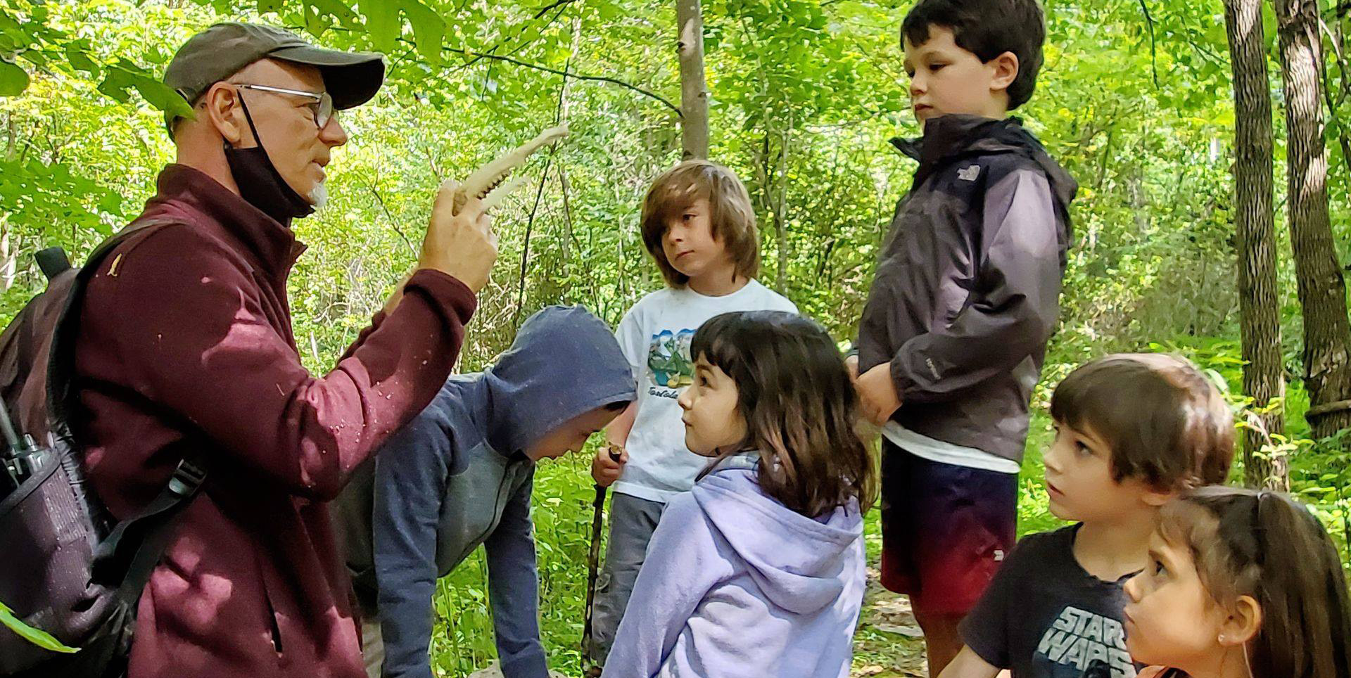 Instructor at homeschool program holding found jaw bone talking with students in forest