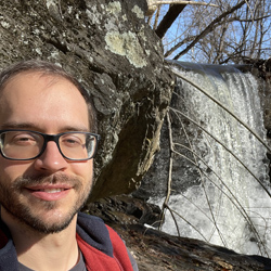 Educator Jacob Reid standing beside a waterfall