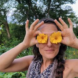 Nature connection mentor Jessica Gifford holding two daisy blossoms up in front of her eyes playfully