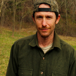 Experienced nature connection mentor Josh Roberts wearing a baseball cap at the edge of the forest