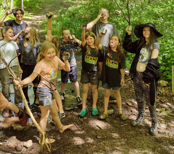 Kids goofing around by the creek with camp cups and making funny faces at Forest Floor Wilderness programs