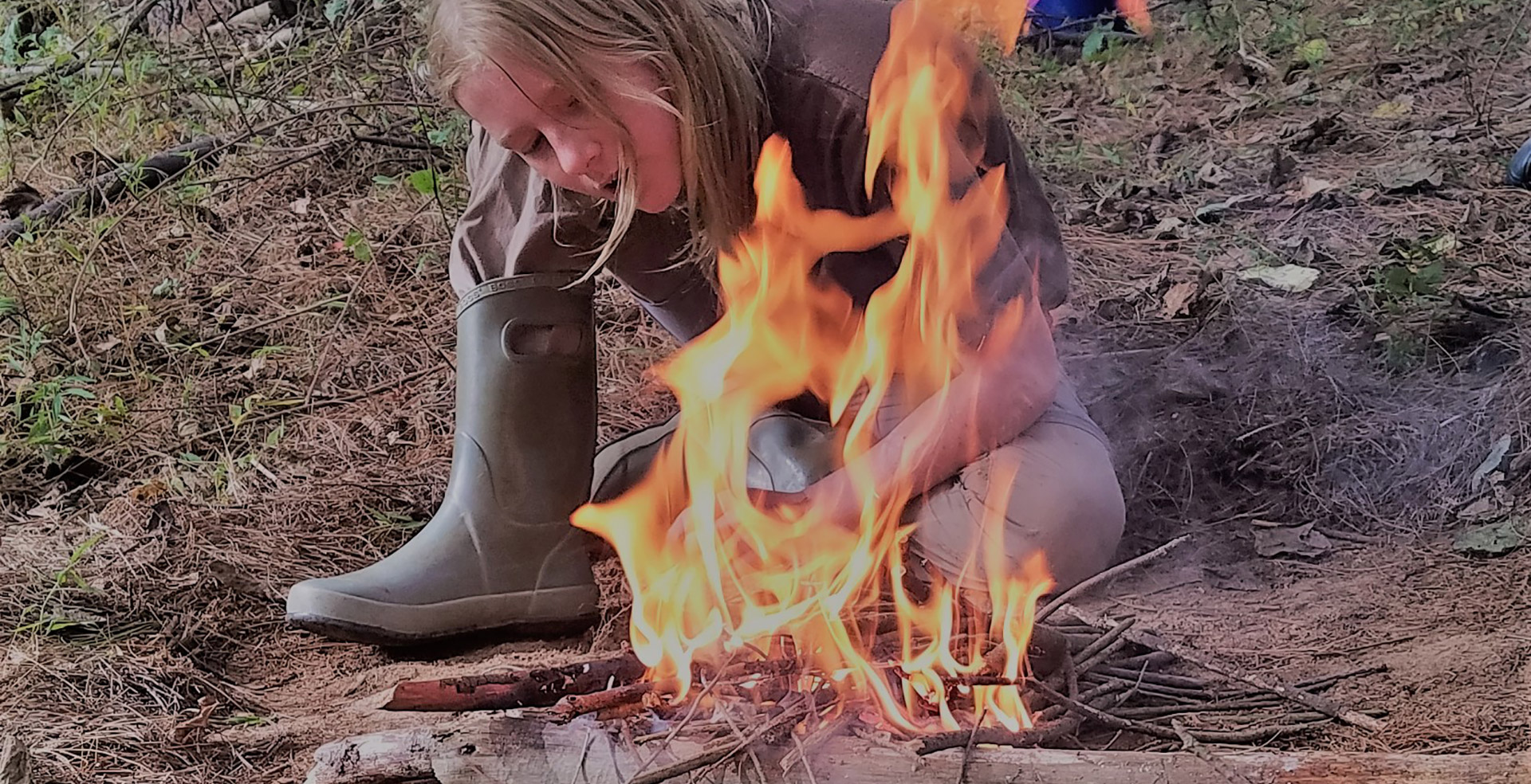 Girl learning to make fire at survival skills summer camp in Asheville