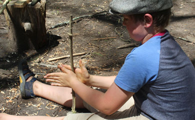 Camper learning to make fire by friction at Asheville day camp for nature connection