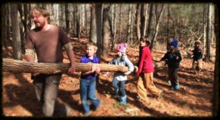 Nature school counselor and children hauling a log for building a primitive structure