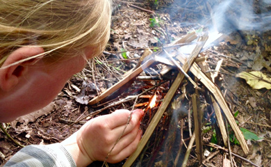 Camper learning to make fire at survival skills summer day camp in forest