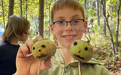 Middle school boy holding up play figures made at Wild Crafters program using sticks and walnut drupes